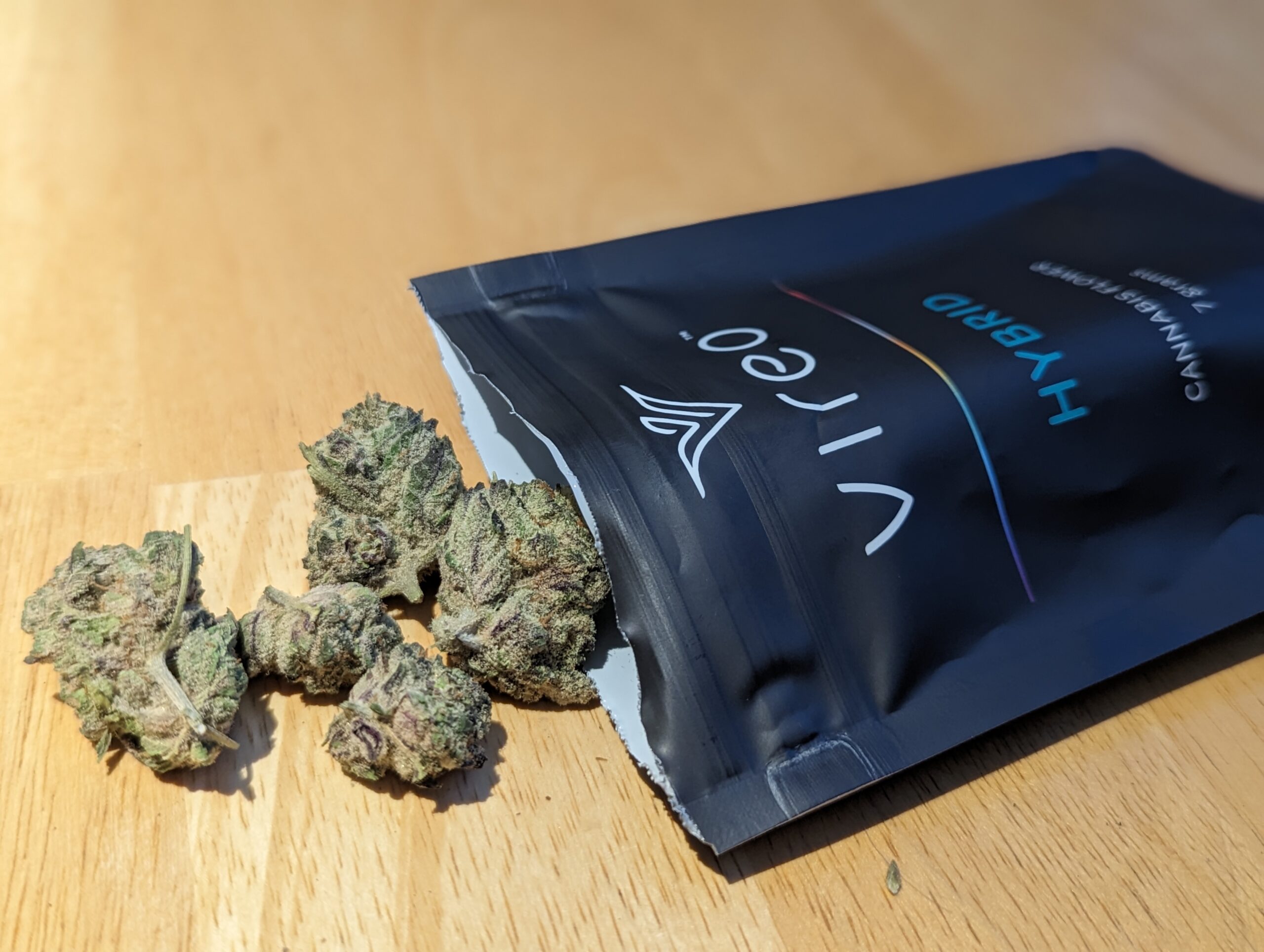 A photo of a package of marijuana flower with several buds spilling onto the table.